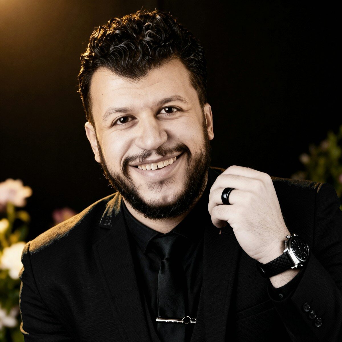 A smiling man in a black suit and tie.